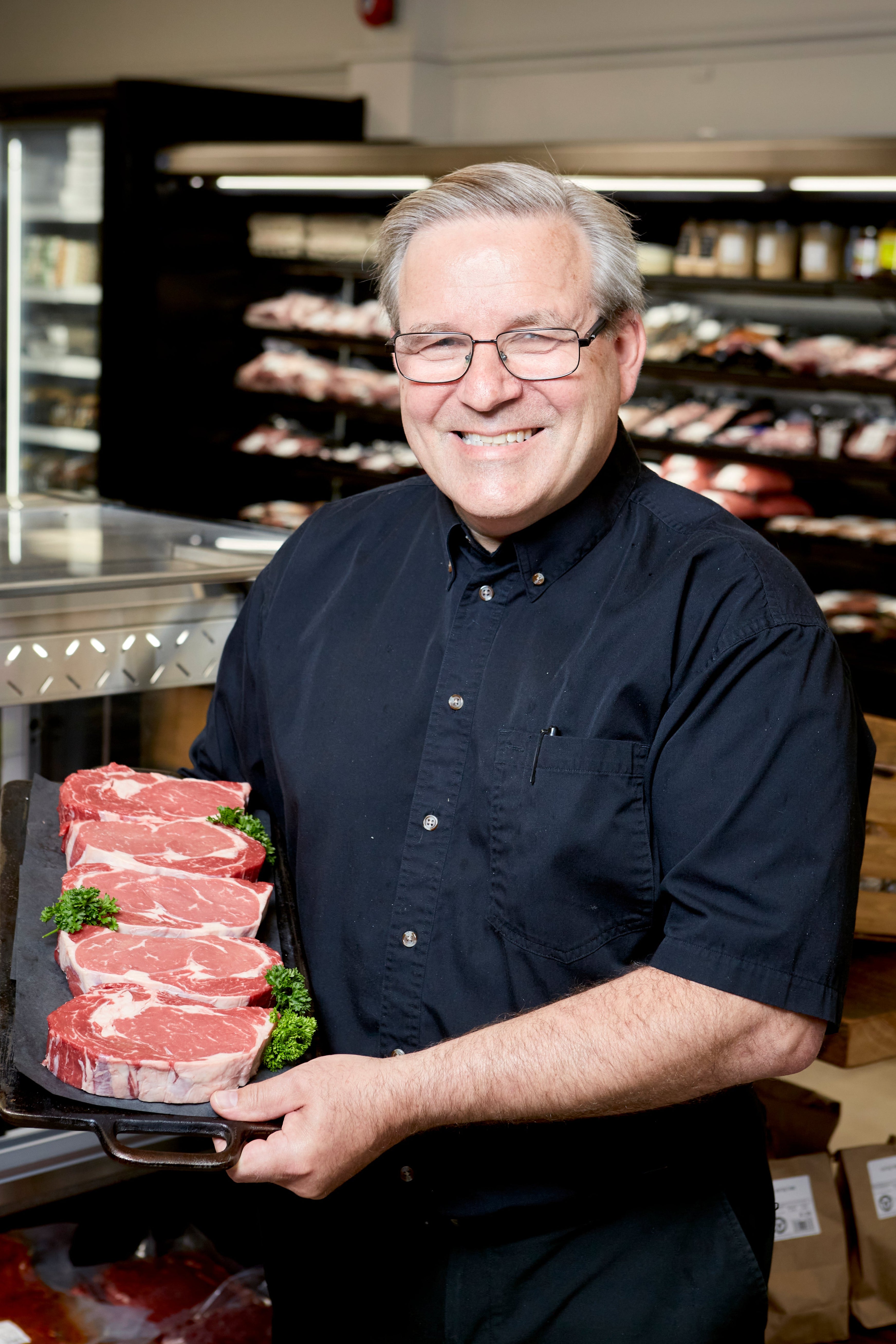 Man holding a tray of steaks in a meat market
