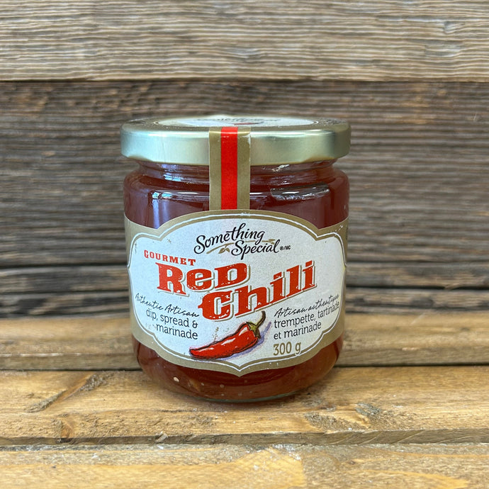 Jar of red chili jam on a wooden surface