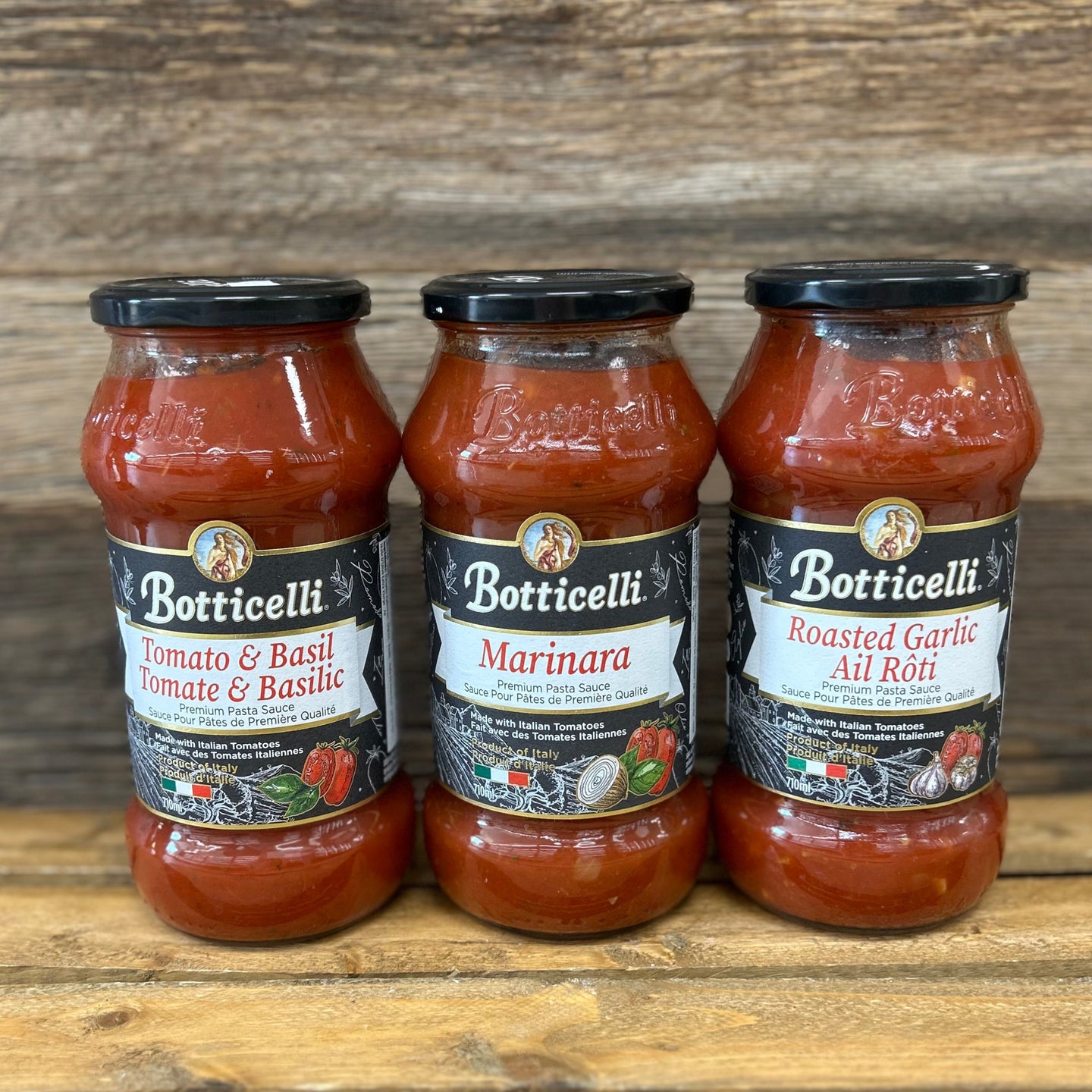 Three bottles of Botticelli pasta sauces on a wooden surface with a wooden background.